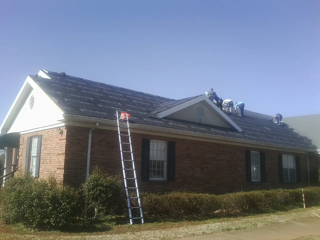 Crew tearing shingles off a brick ranch roof with a ladder set — Metal Roof Repair work by our crew in Lexington